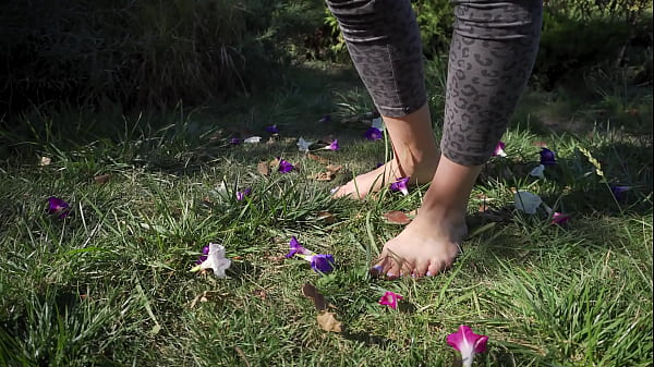 Sexy feet with long toes crushing flowers outdoors 